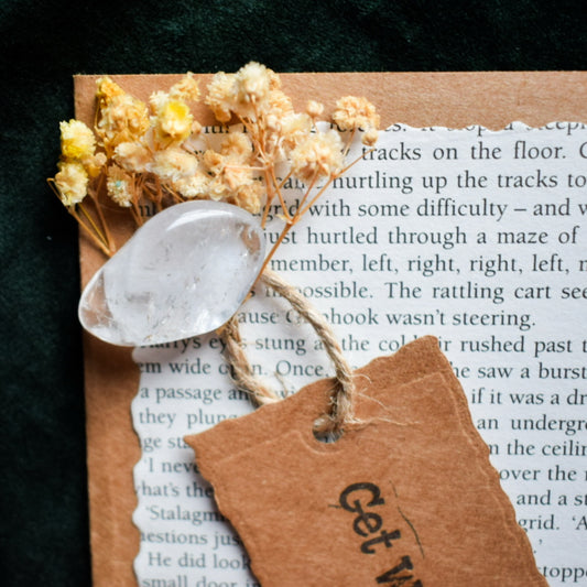 Decorative element with dried flowers, a clear quartz, and a tag on a book page.