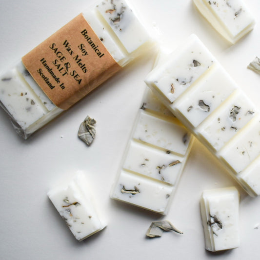 White wax melts with visible herbs on a white surface, with a label indicating 'Sage & Sea' scent.